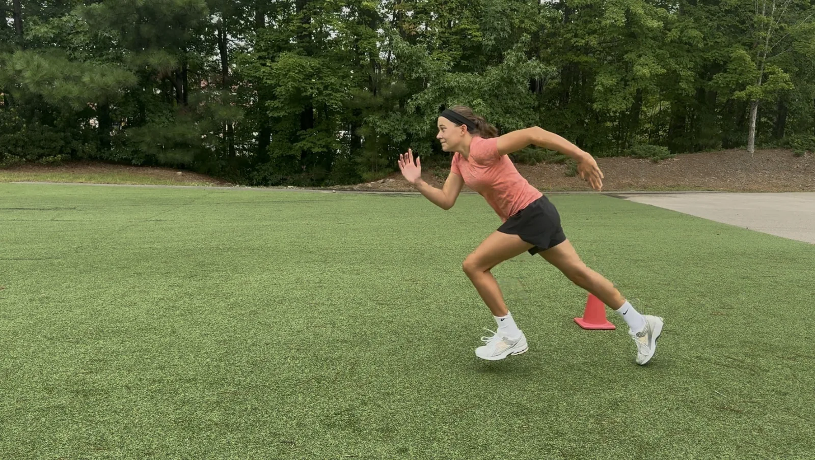 A soccer athlete driving out of her first step past a cone on the grass