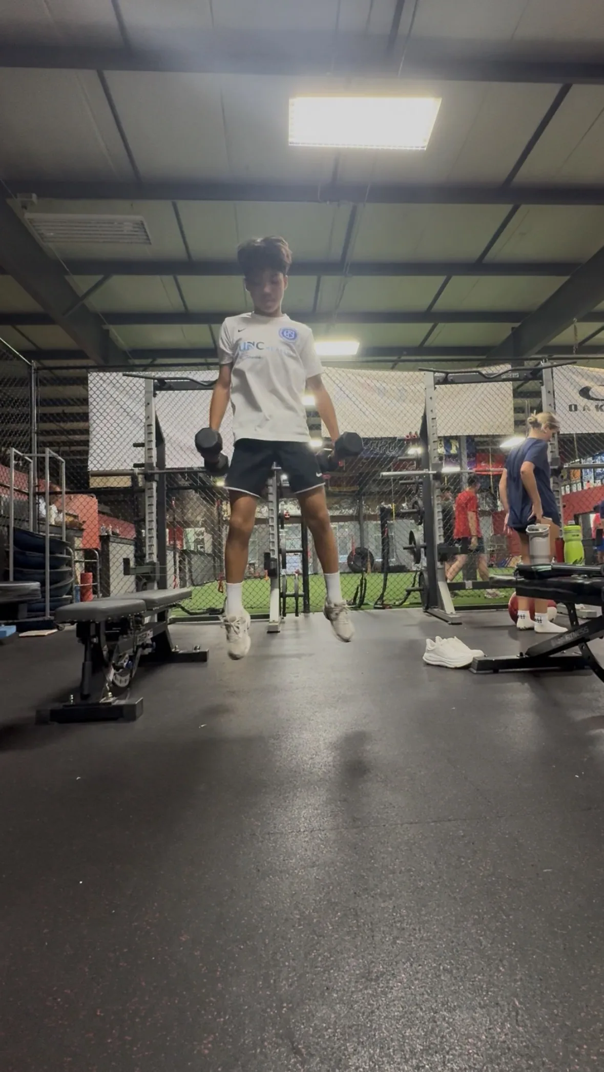 A soccer athlete at the top of a jump holding dumbbells at his sides