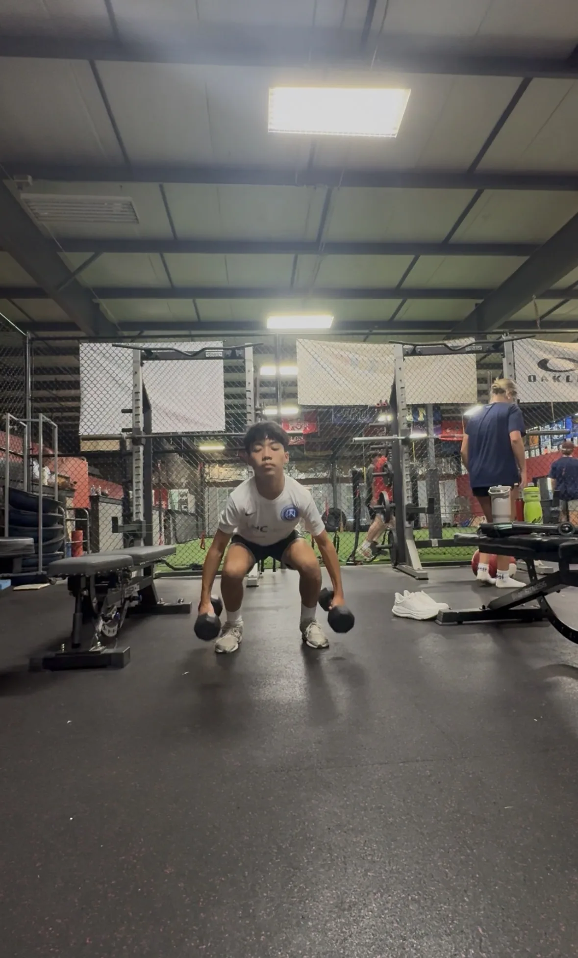 A soccer athlete absorbing a landing with dumbbells at his sides, knees tracking forward